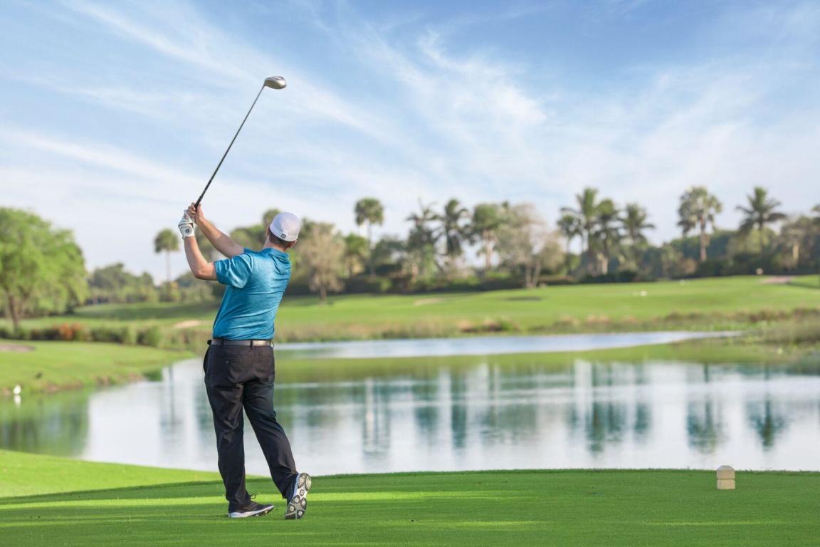 Golfer teeing off over a lake at Boca West Country Club in Boca Raton
